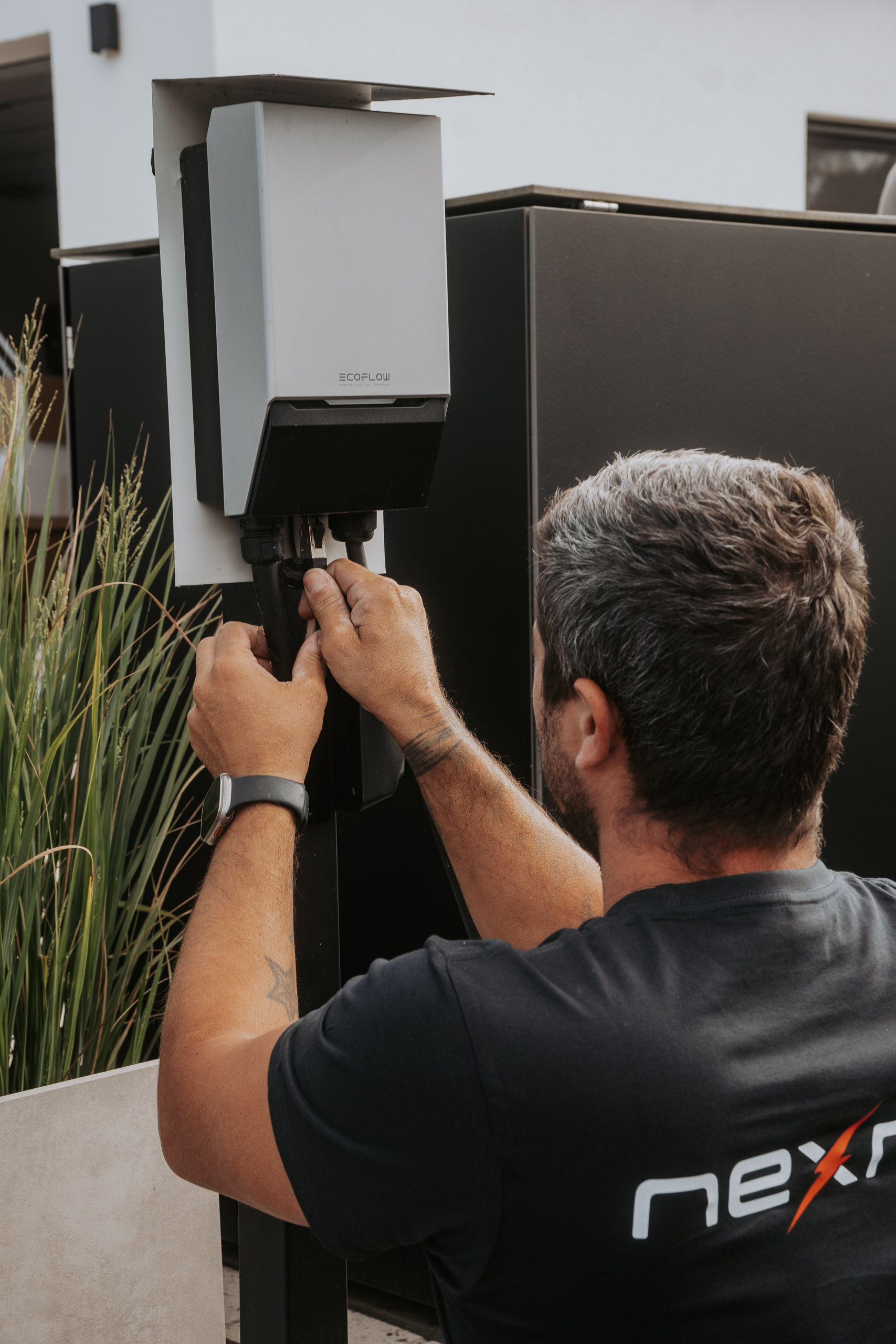 Ein Techniker im Nexron-Shirt schließt im Außenbereich die Anschlüsse an einer freistehenden EcoFlow-Wallbox an.