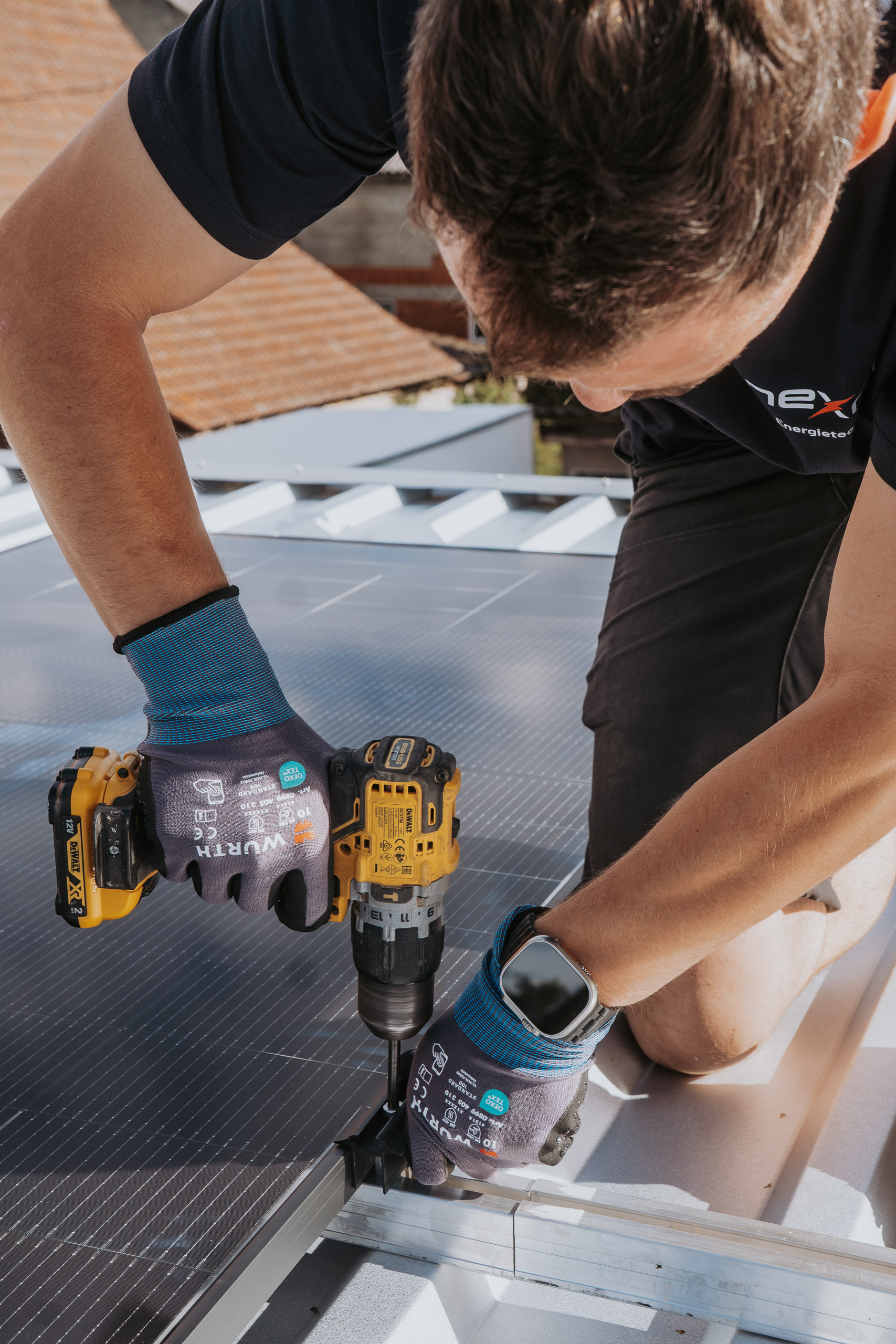 Handwerker von Nexron Energietechnik montiert ein Photovoltaik-Modul mit einem Akkuschrauber auf einem Dach.