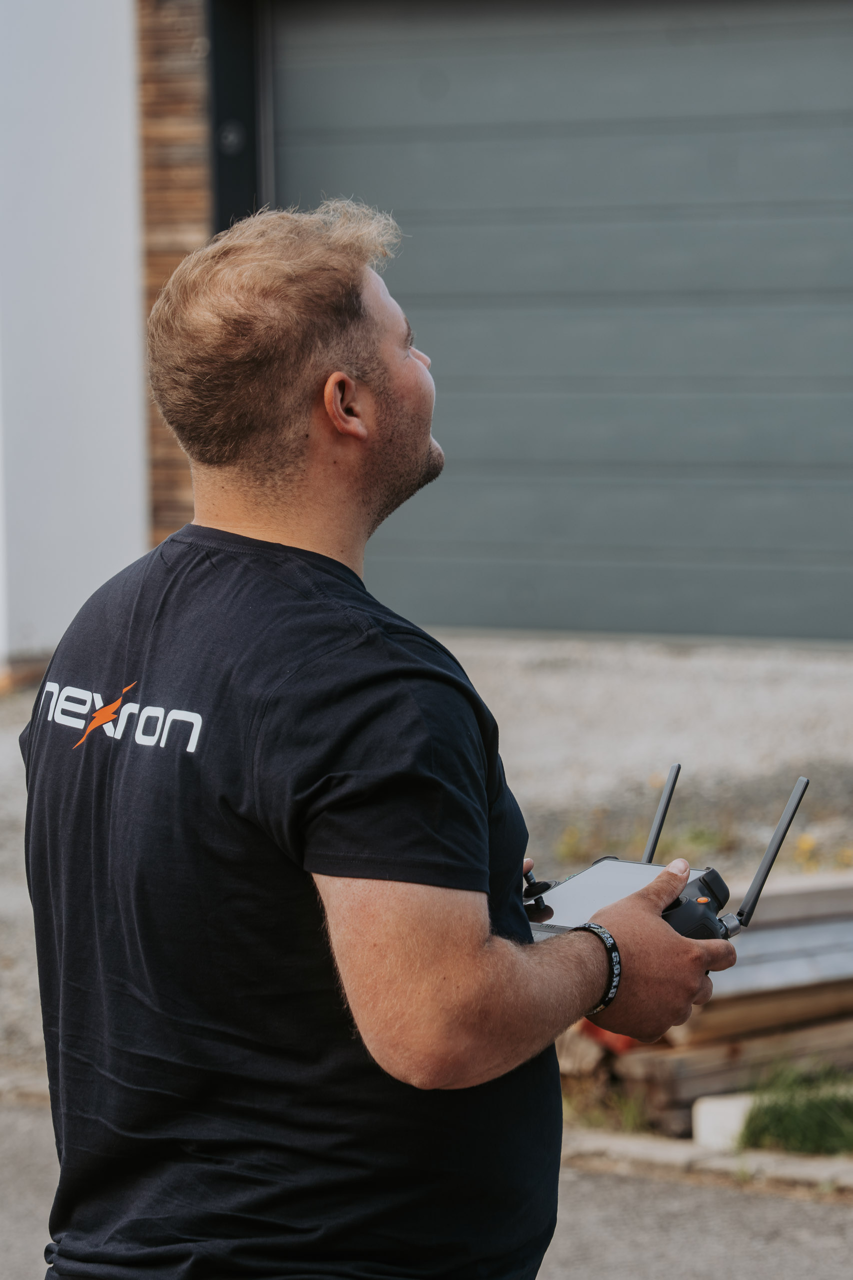Ein Nexron-Mitarbeiter steuert von unten mit einer Fernbedienung eine Drohne zur Gebäudeinspektion und blickt dabei nach oben.