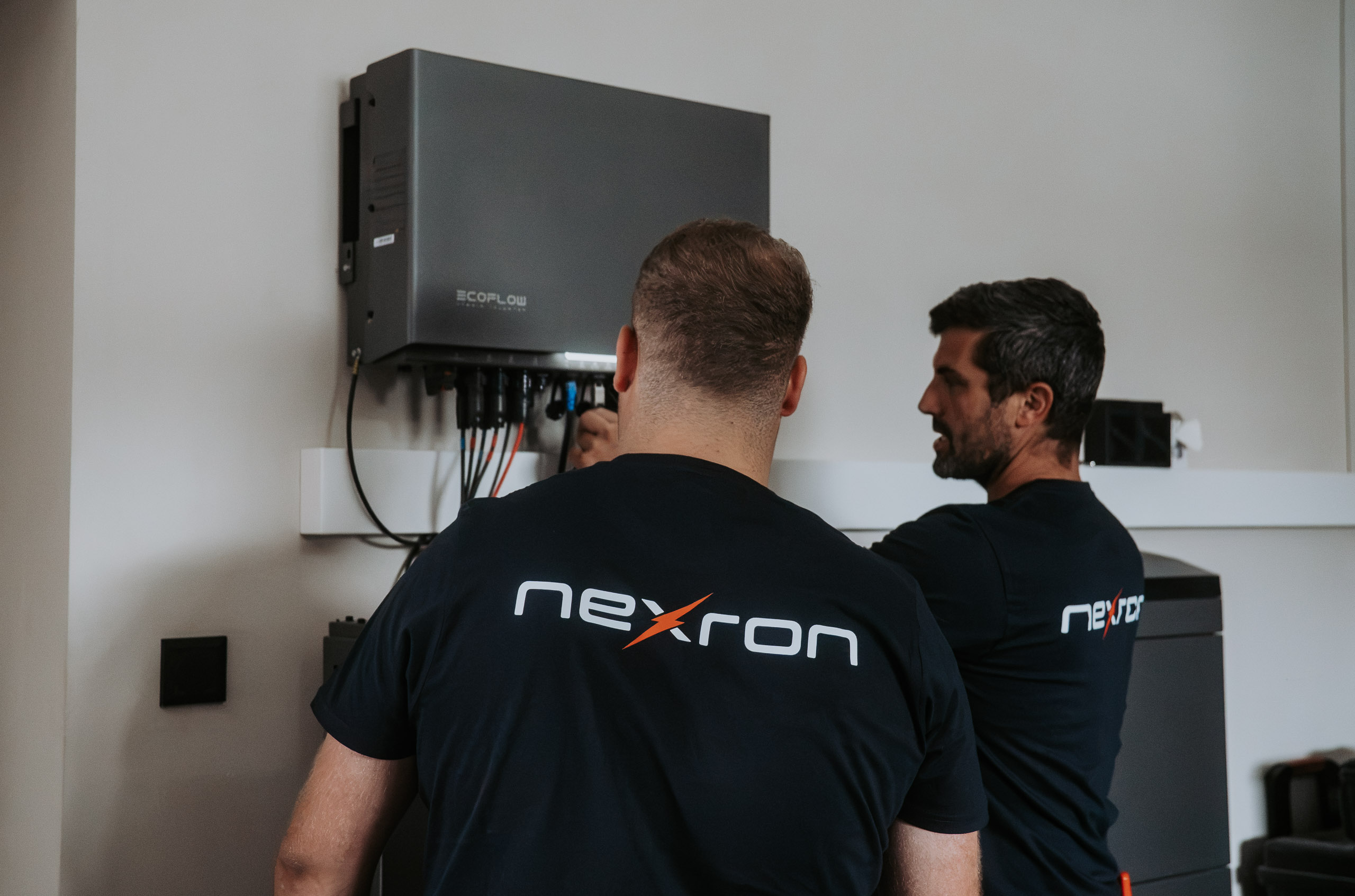 Zwei Techniker in Nexron-Arbeitskleidung montieren einen  EcoFlow Spiecher.