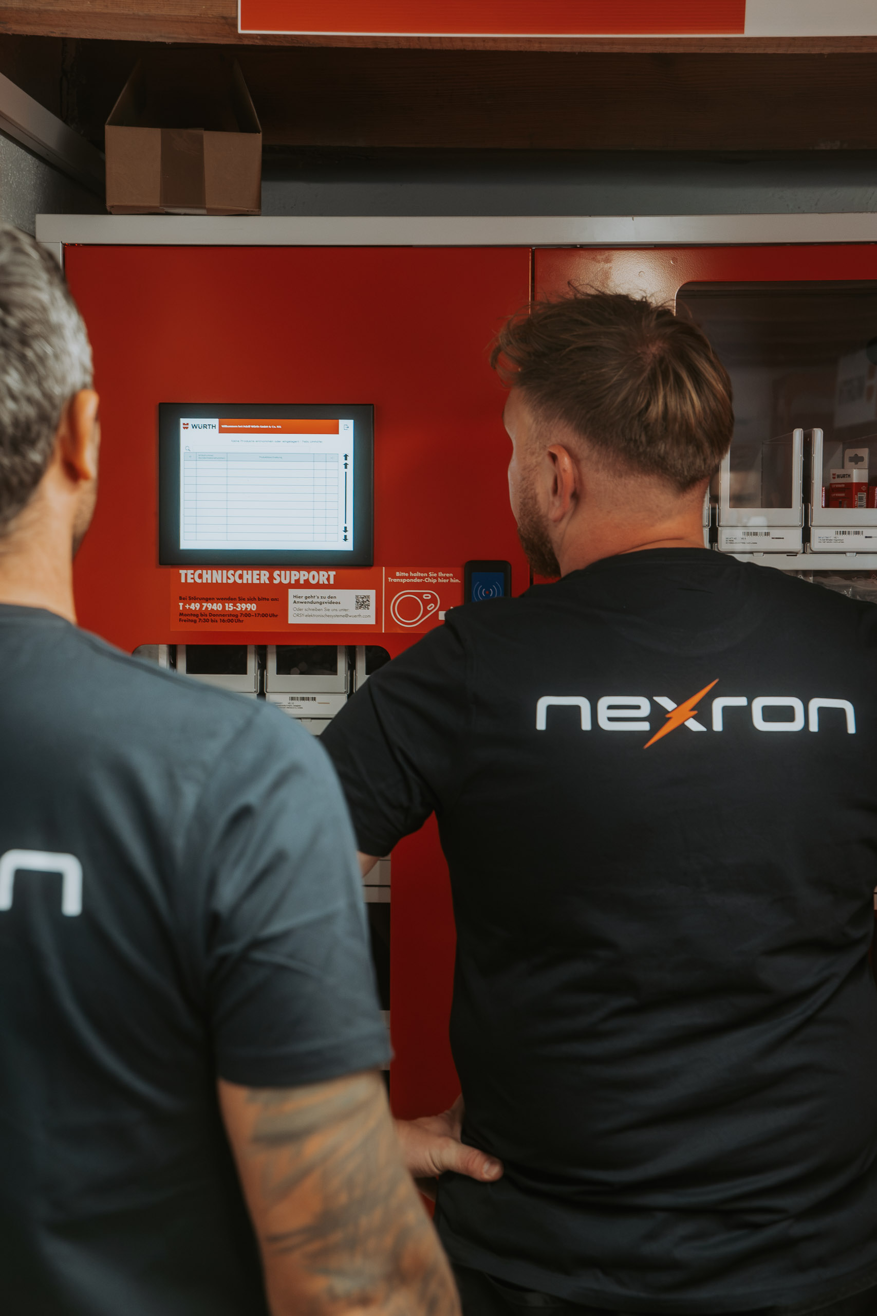Zwei Nexron-Mitarbeiter bedienen den Touchscreen eines roten Würth-Materialausgabeautomaten im Lager.