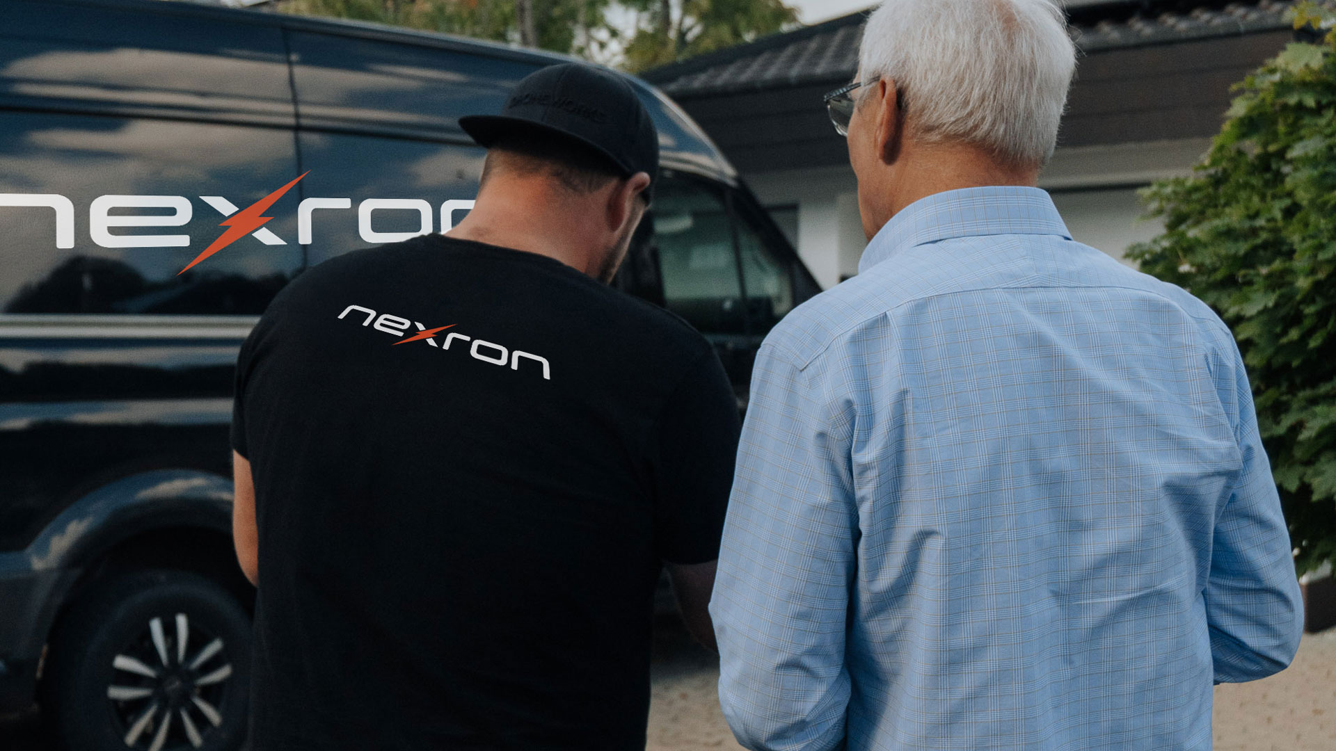 Nexron-Mitarbeiter im persönlichen Beratungsgespräch mit einem Kunden vor einem Firmenfahrzeug und einem Wohnhaus.