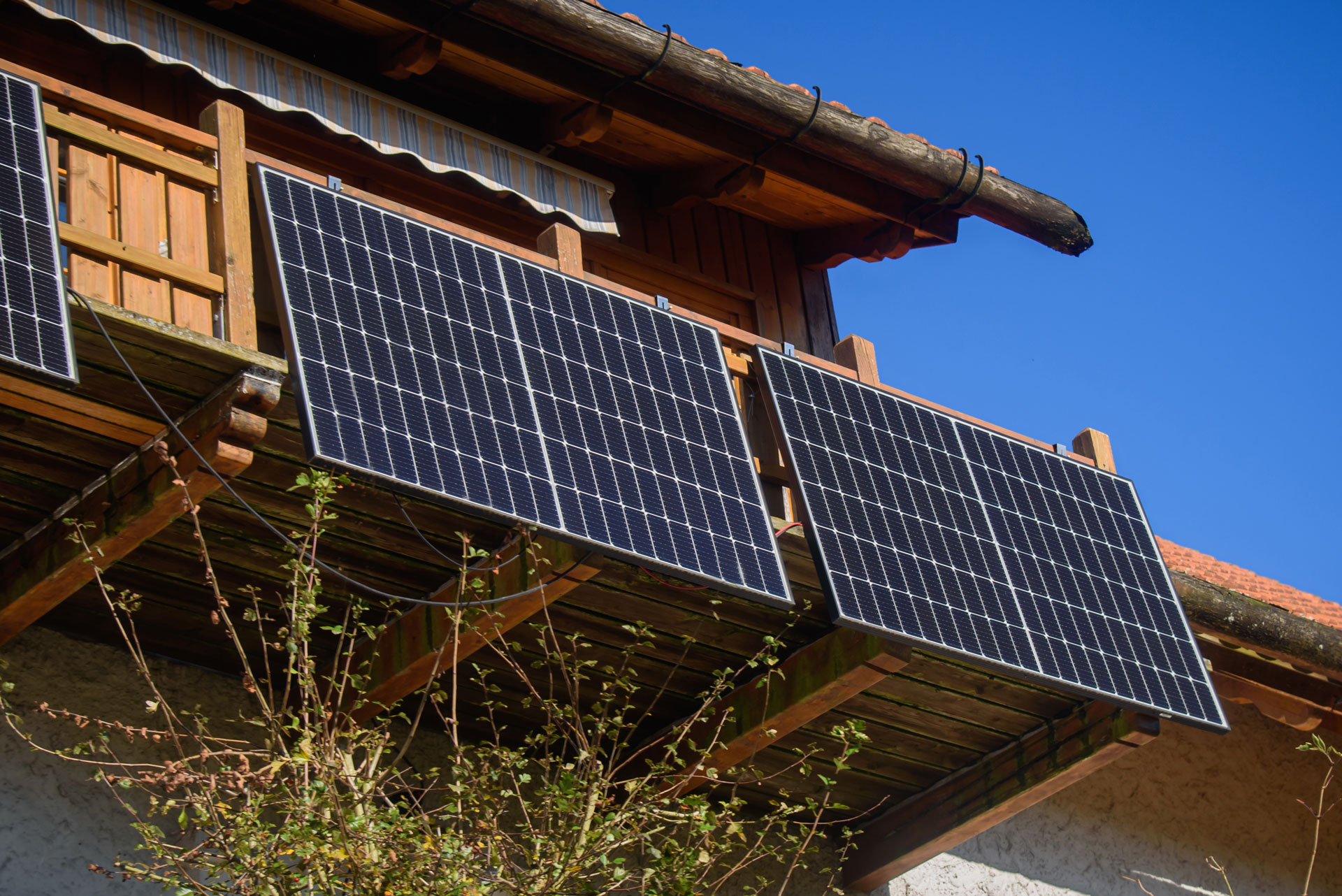 Mehrere Solarmodule sind am Holz-Balkon eines Hauses montiert, vor blauem Himmel.
