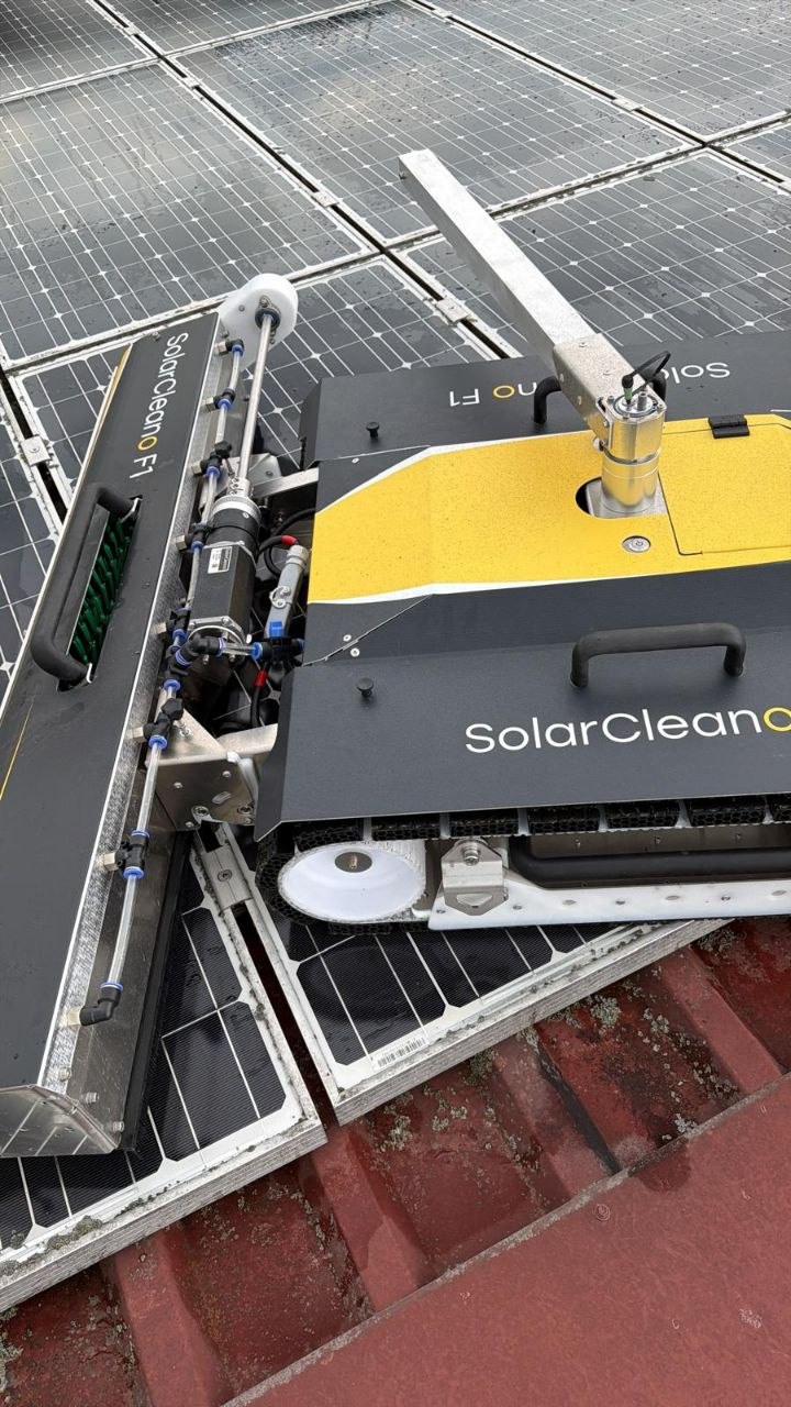 Schwarz-gelber SolarCleano F1 Reinigungsroboter mit Bürstenwalze steht auf einer Photovoltaikanlage auf einem Ziegeldach.