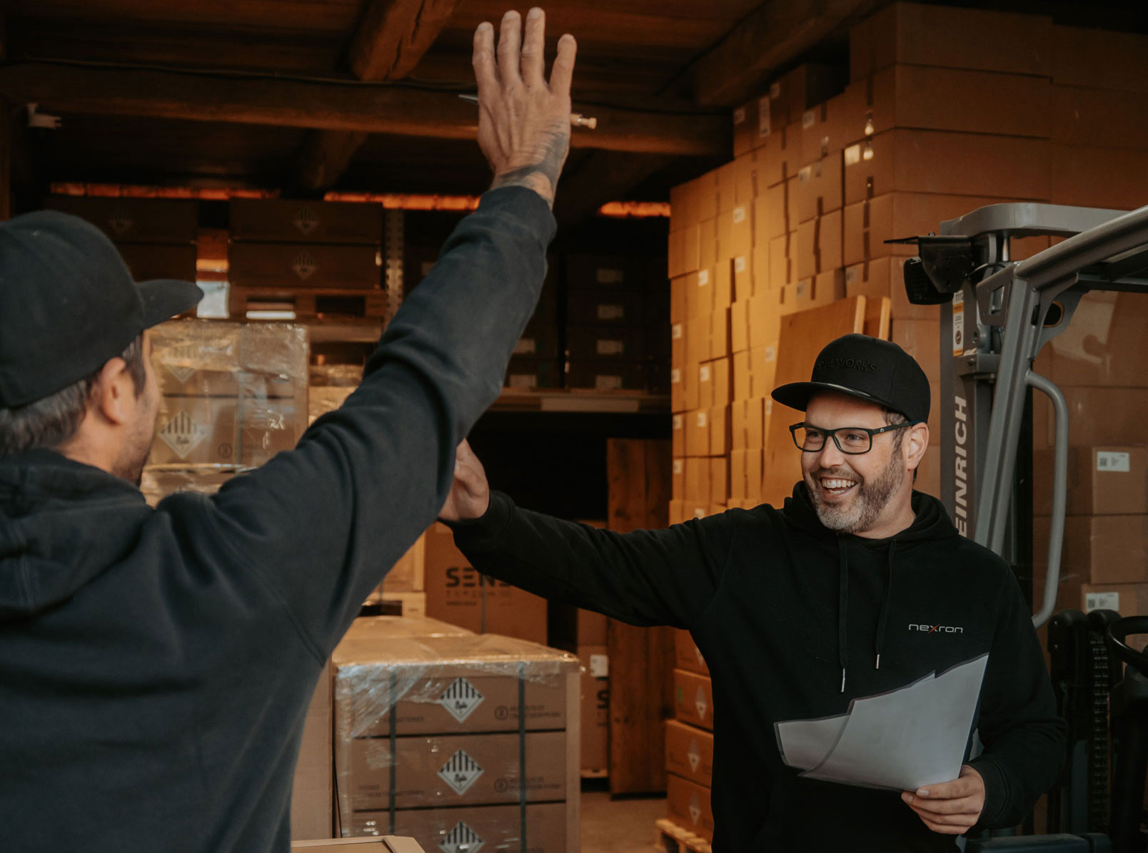 Zwei engagierte Mitarbeiter von Nexron geben sich im Logistikzentrum ein High-Five bei der Arbeit mit Komponenten für erneuerbare Energien.